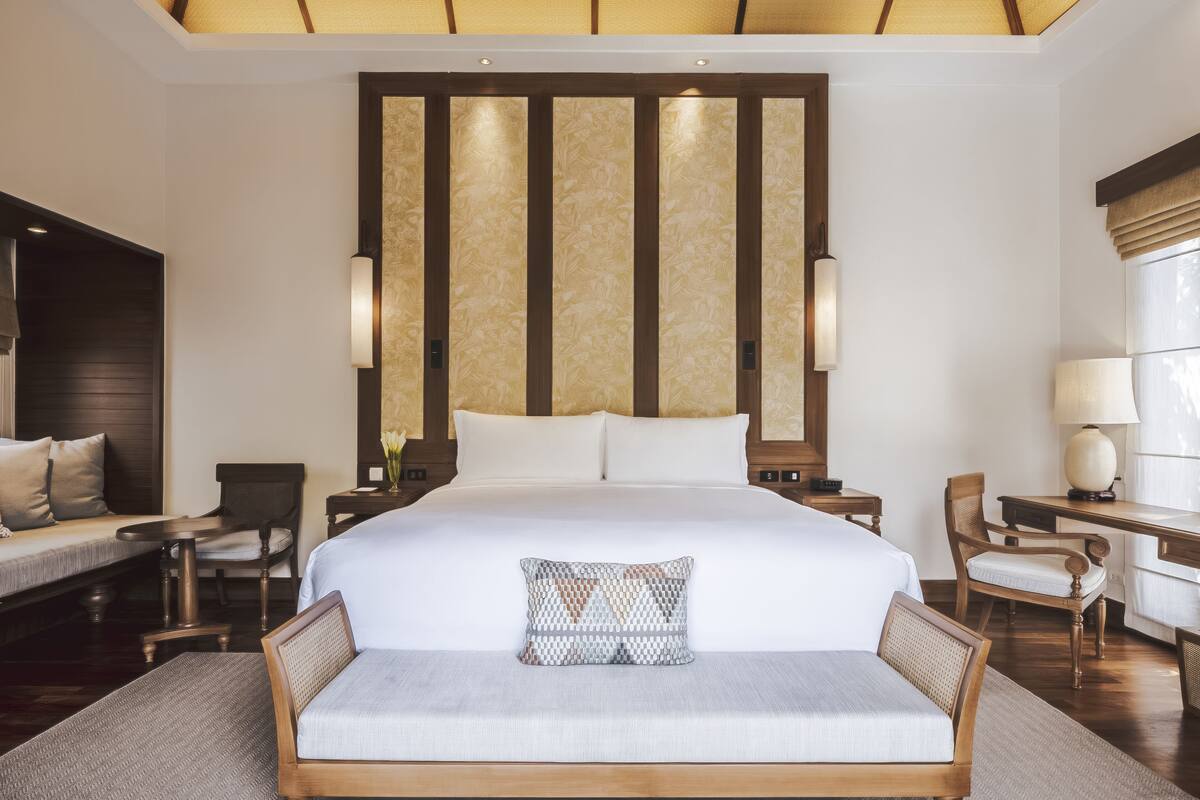 Ein Hotelzimmer mit einem großen Bett, einem Nachttisch mit Lampe, einem Sessel und einem Schreibtisch ebenfalls mit Lampe.