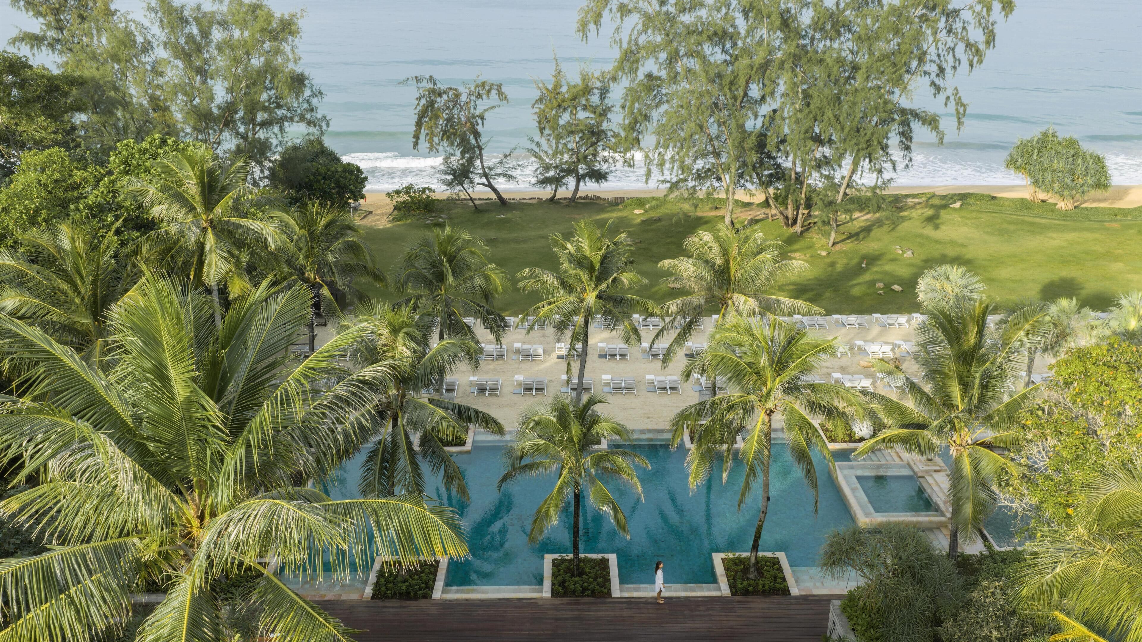 Un resort con piscina, palmeras y vista a la playa.