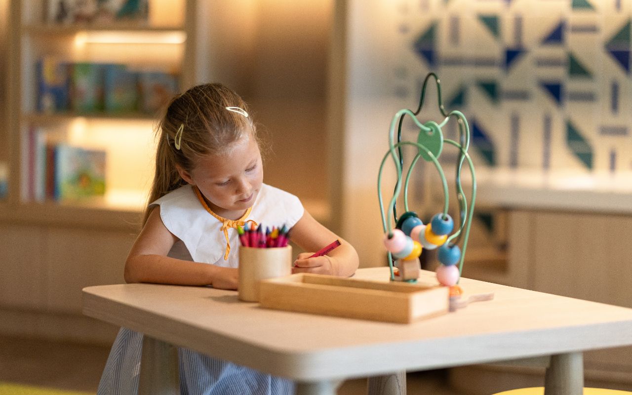 A child sitting at a table with a toy and a container of crayons.