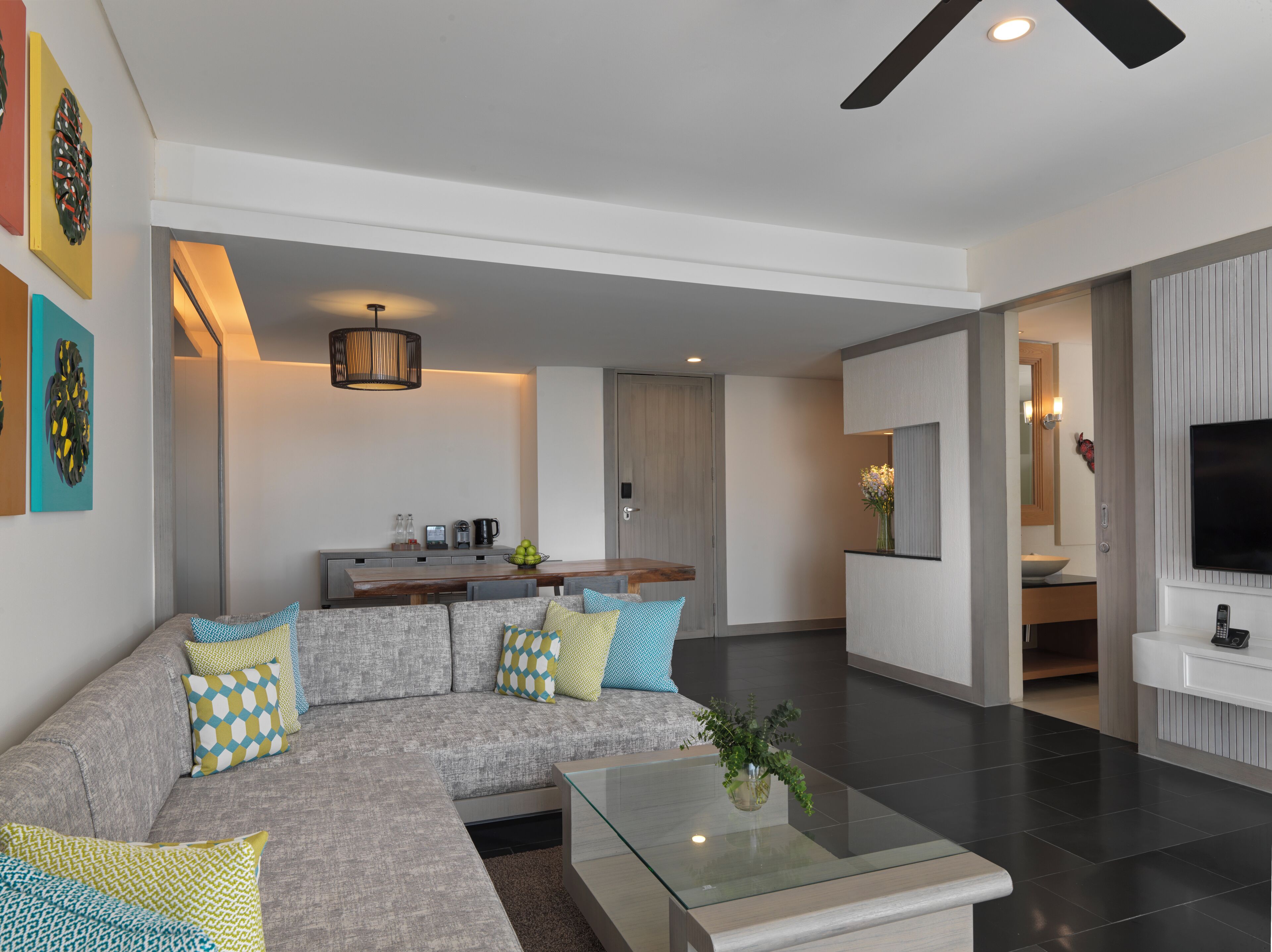 A modern living room with a sectional sofa, a glass coffee table, and a kitchen area in the background.