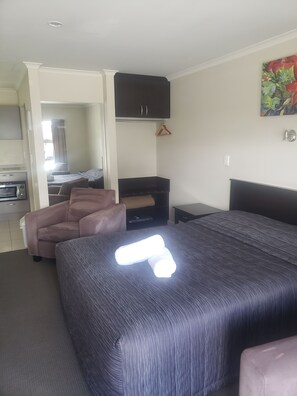 A hotel room with a bed, a sofa, a wardrobe, a small table, and a TV. - St John's Court Motel (Milton)