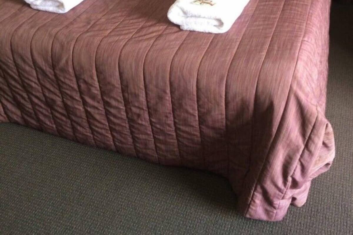 A neatly made bed with a brown quilt and two white towels with bottles on them.