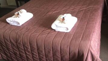 A neatly made bed with a brown quilt and two white towels with bottles on them.