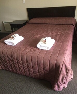 A neatly made bed with a brown quilt and two white towels with bottles on them.