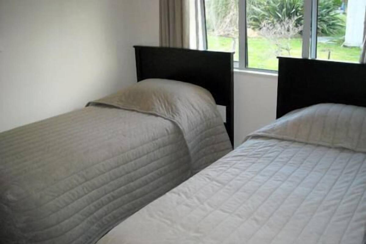 Two single beds with headboards, a window with a view of greenery, and a plain wall.