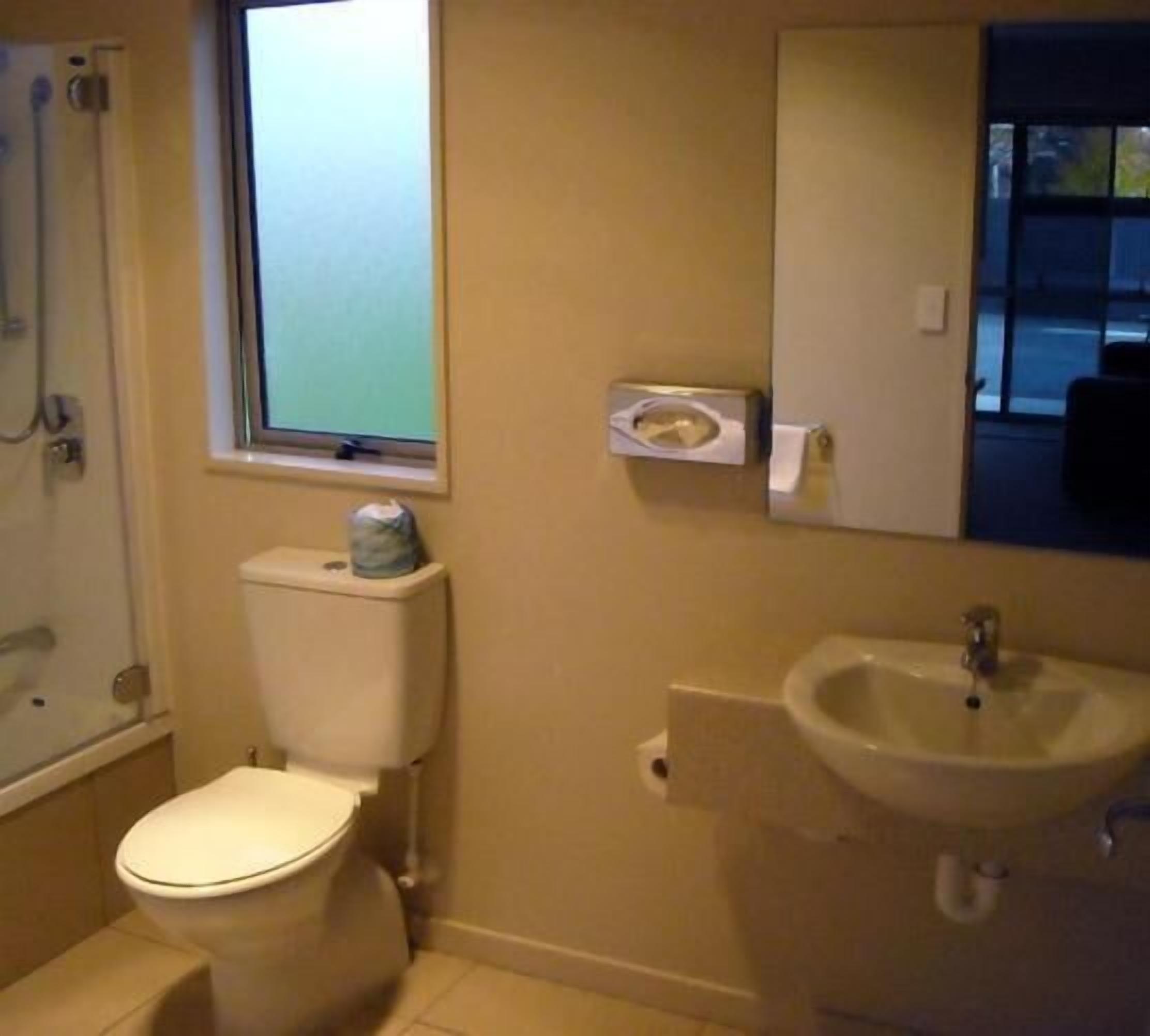 A bathroom with a toilet, a sink, and a window above the toilet.