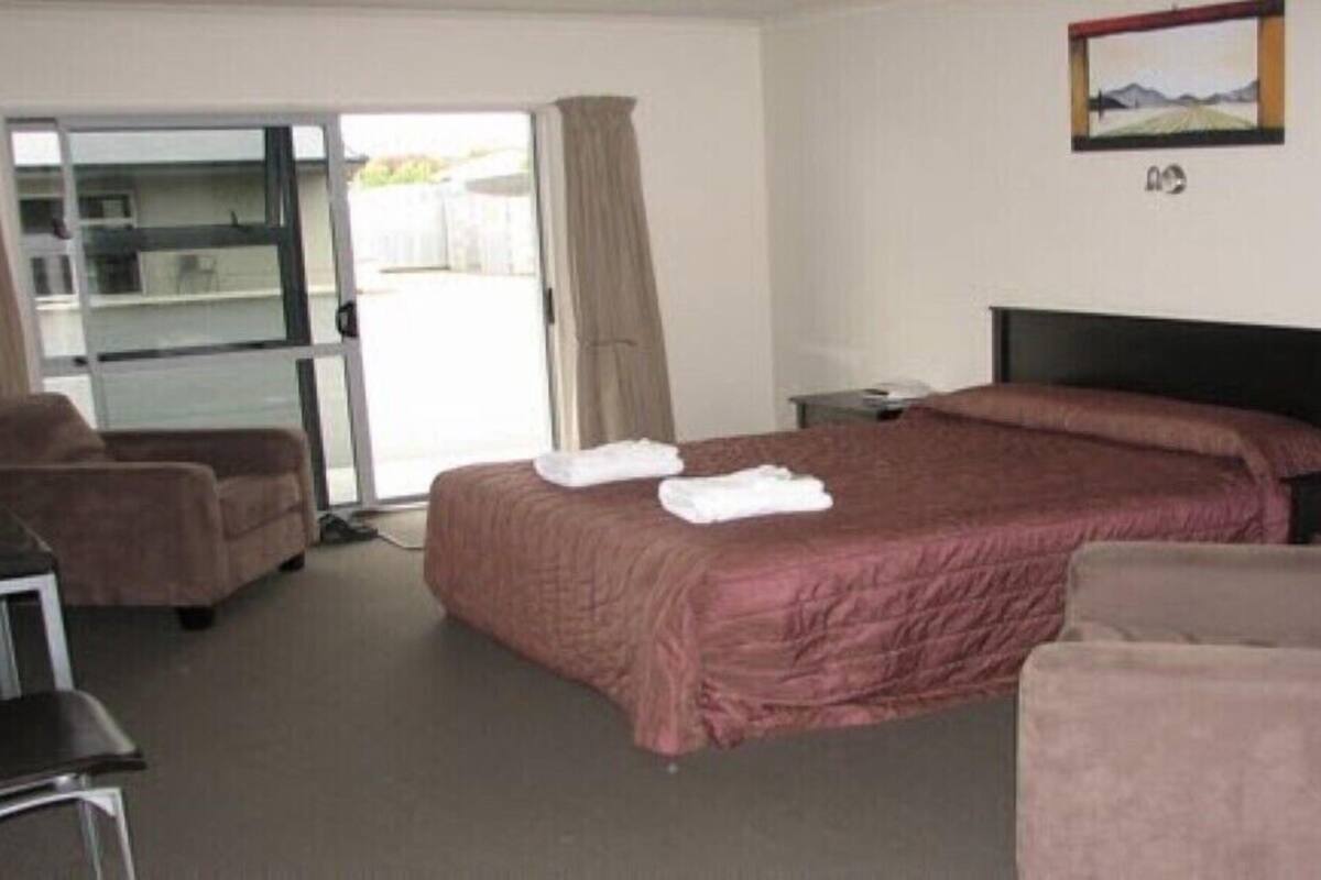 A hotel room with a bed, a desk, a chair, a TV, and a sliding glass door to the outside.