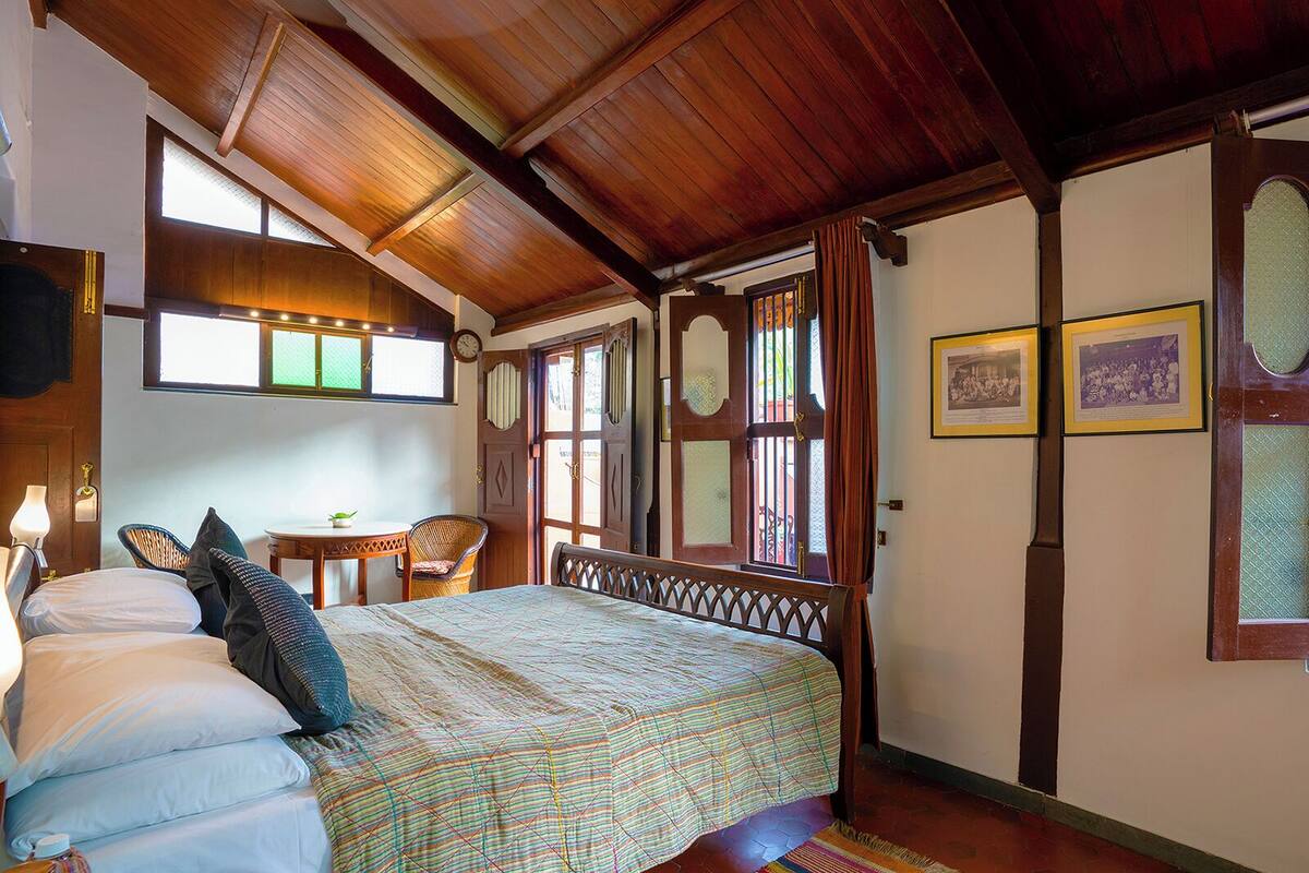 A cozy bedroom with a wooden ceiling, a bed with a patterned bedspread, a small table, and chairs.