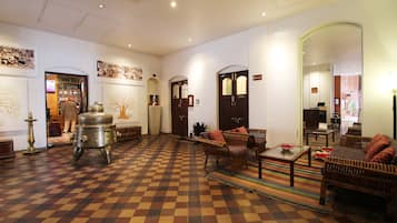 A checkered floor, wicker furniture, and a large metal stove in a room with white walls and wooden doors.