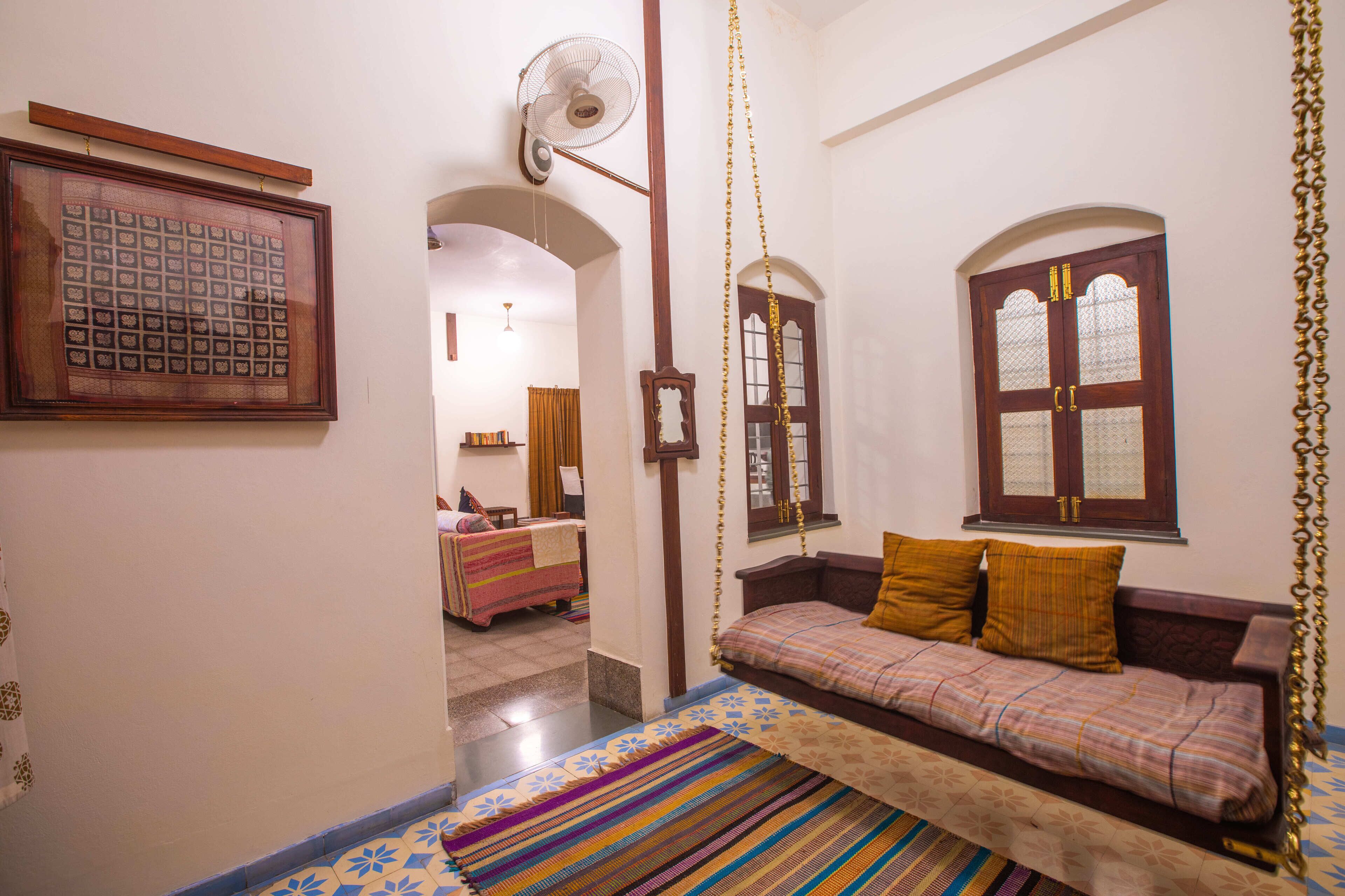 A room with a swing bed, a patterned rug, a wooden door with glass panels, and a fan.