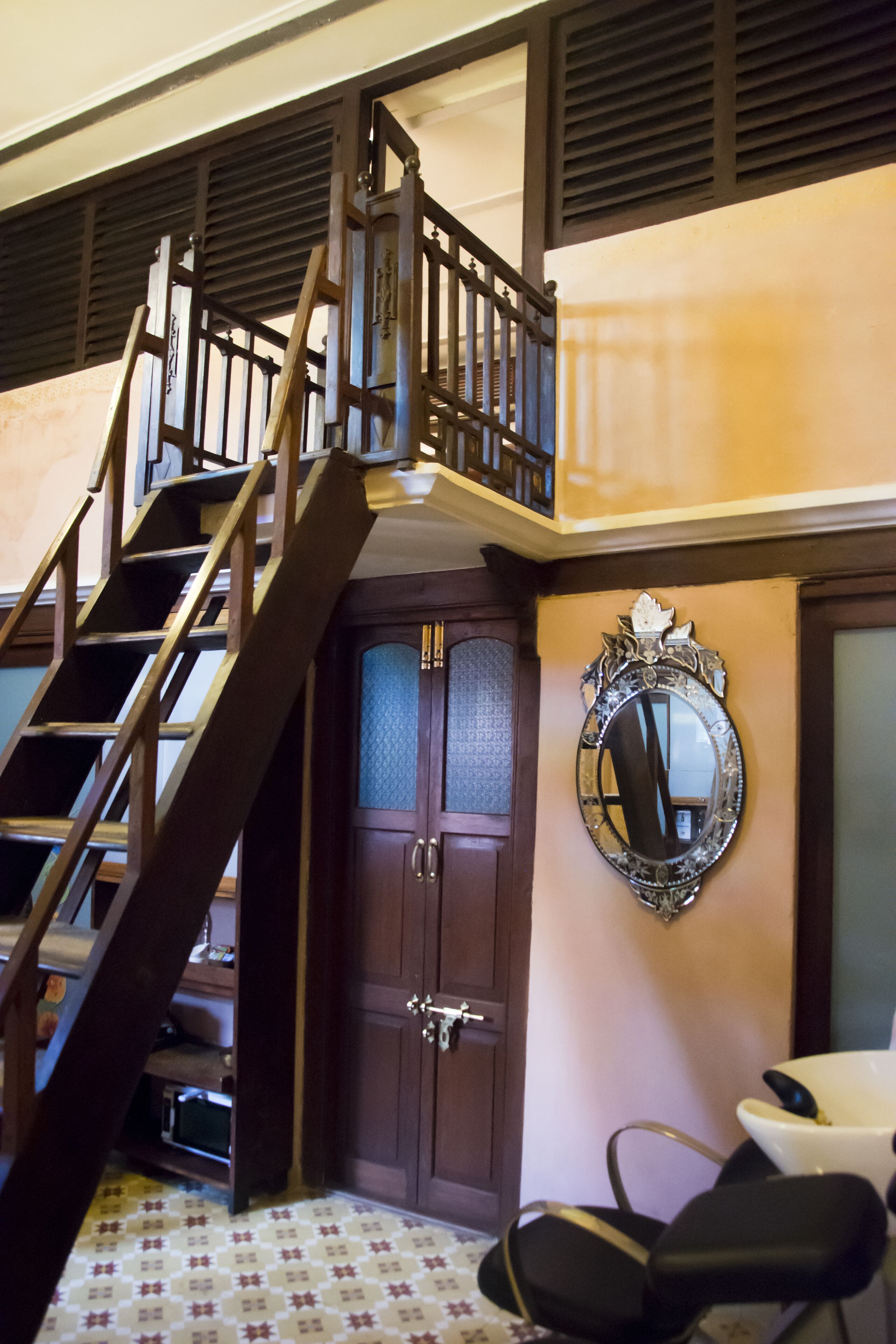 Una escalera con barandilla de madera que lleva a un rellano, una puerta de madera con panel de vidrio y un espejo fijado a la pared.