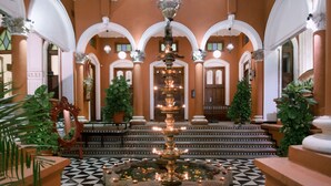 A grand lobby with a central fountain, ornate columns, and a checkered floor.