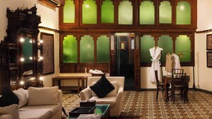 A traditional room with a large mirror, a sofa, a small table, and a chair. There is a window with green glass panes and a patterned floor.