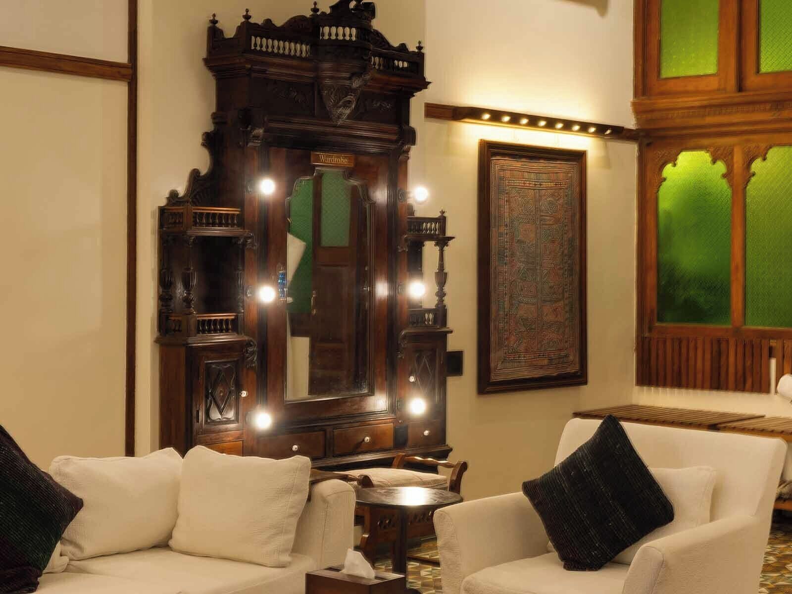 A room with a large ornate mirror, two white armchairs with black cushions, and a small table.