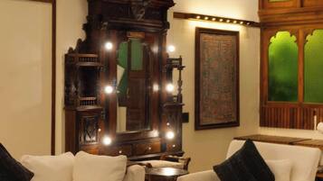 A room with a large ornate mirror, two white armchairs with black cushions, and a small table.