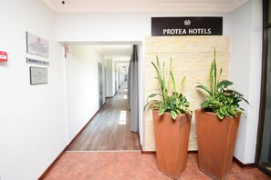 A hotel lobby with a sign reading "Protea Hotels," a corridor with doors, and two large potted plants. - Protea Hotel by Marriott Harrismith Montrose (Maluti a Phofung)