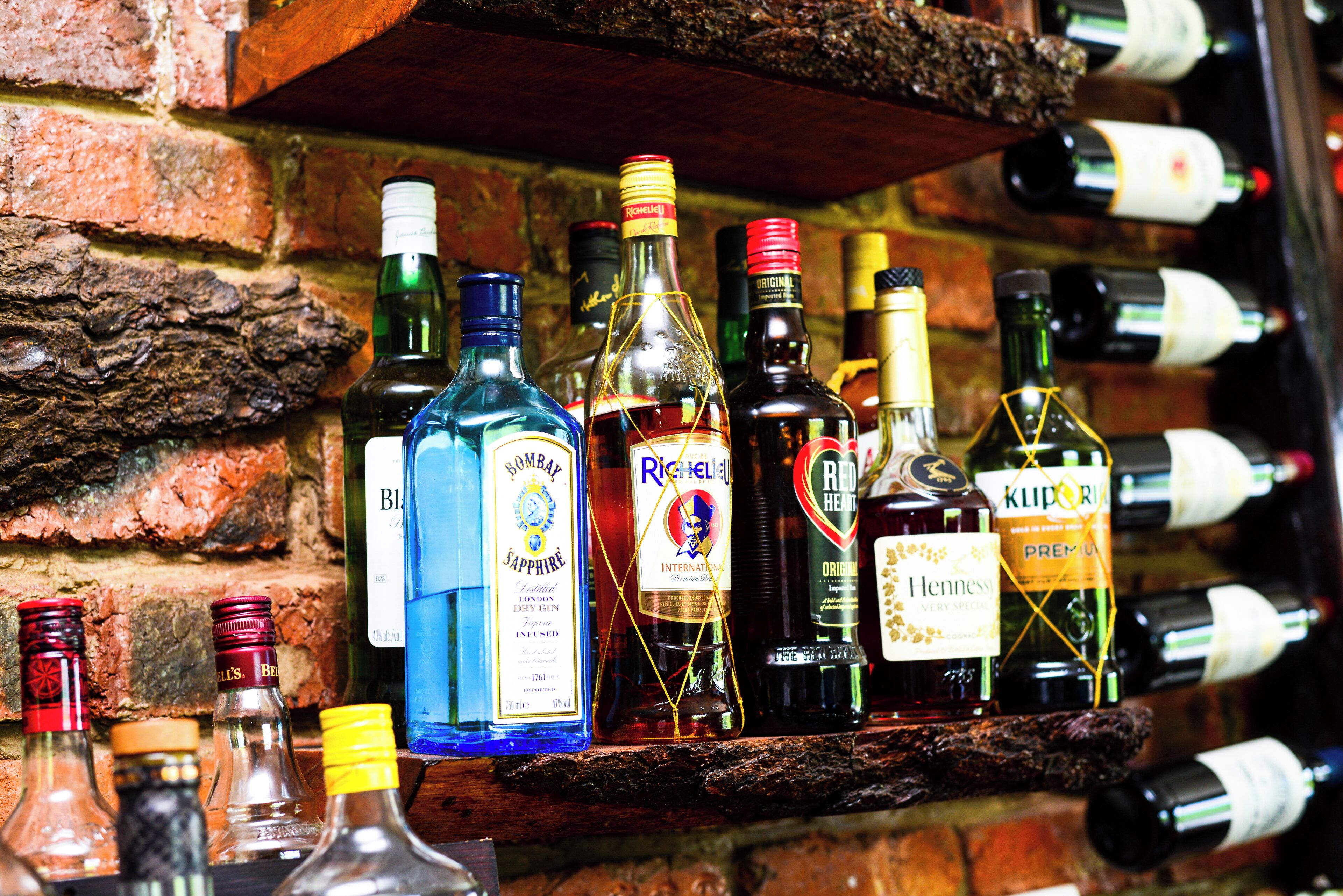 Diverses ampolles d'alcohol exposades sobre una prestatgeria de fusta davant d'una paret de maó.