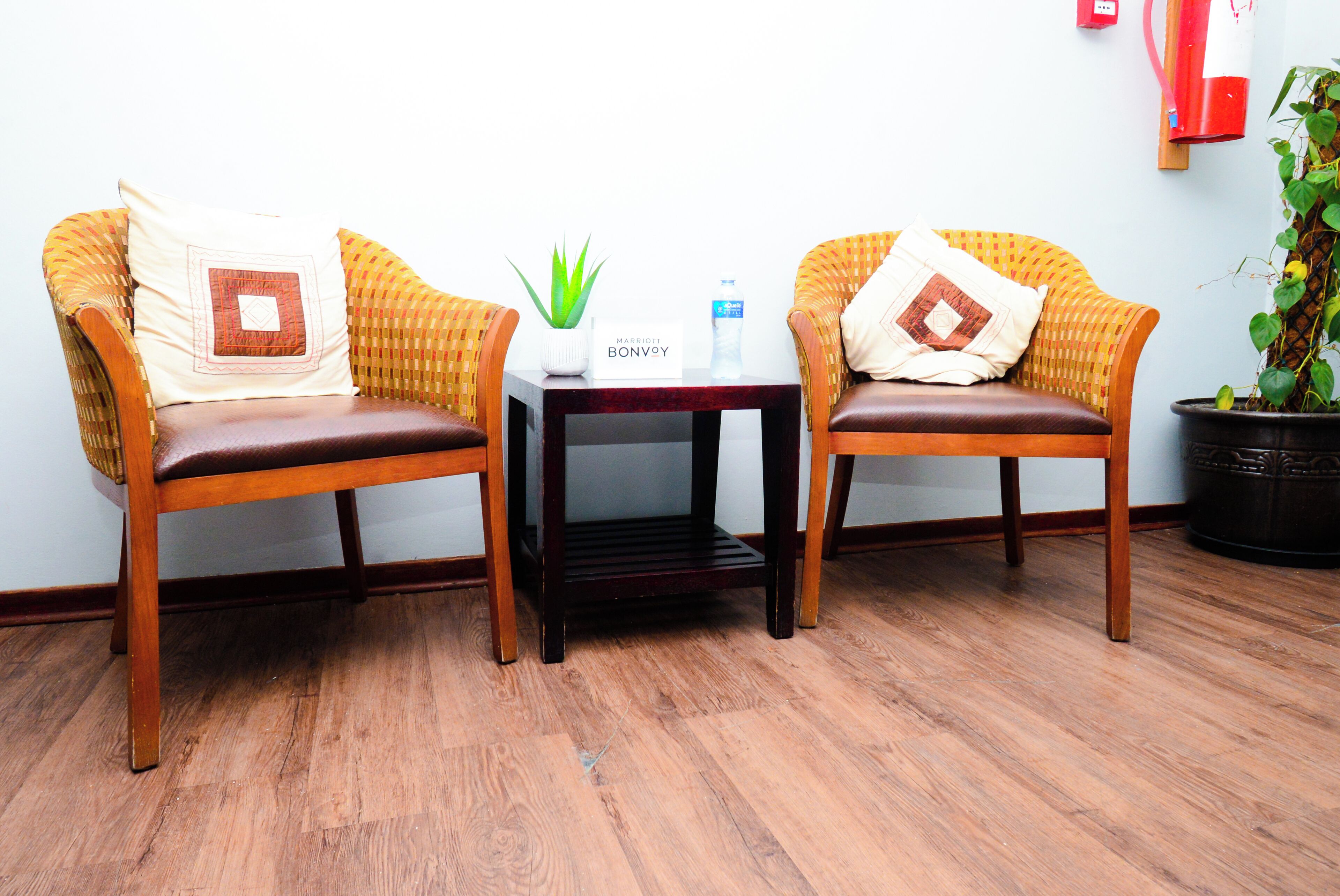 Two wicker chairs with cushions, a small table with a plant and a water bottle, and a sign reading "MARRIOTT BONVOY".