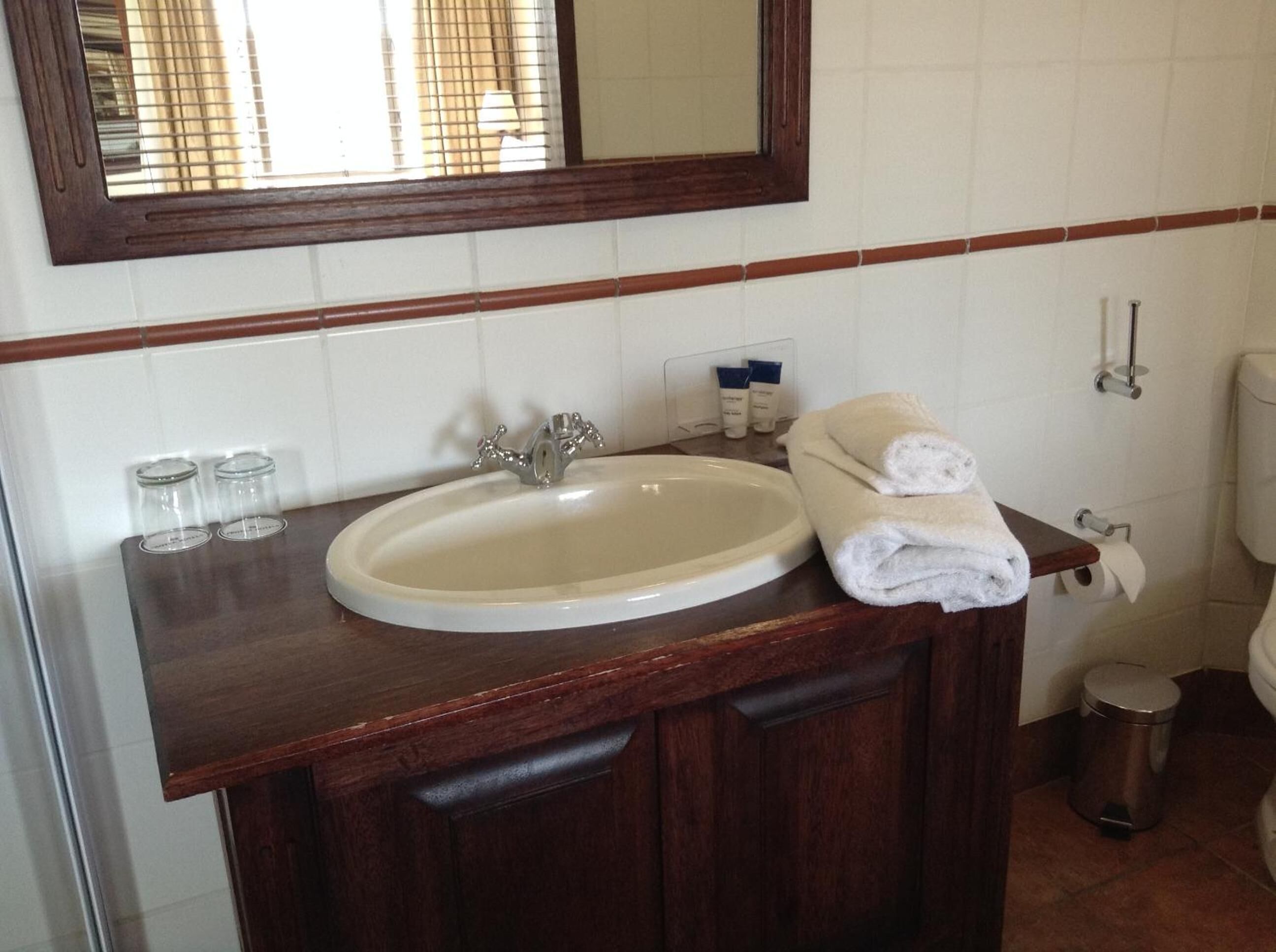 A bathroom with a white sink, wooden vanity, a mirror, and a toilet.