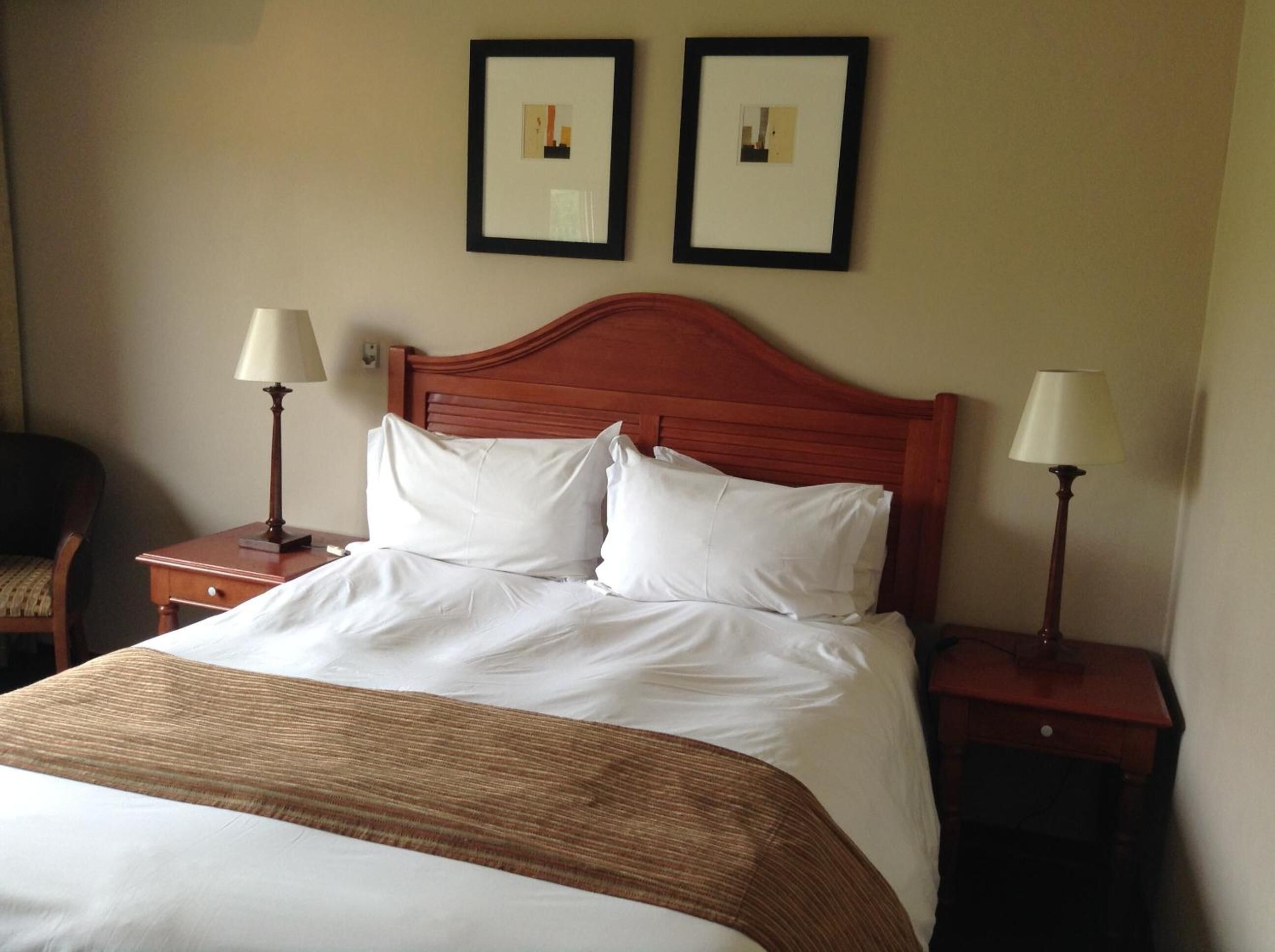A neatly made bed with a wooden headboard, two bedside tables with lamps, and two framed pictures on the wall.