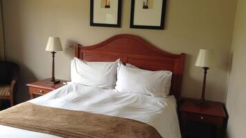 A neatly made bed with a wooden headboard, two bedside tables with lamps, and two framed pictures on the wall.
