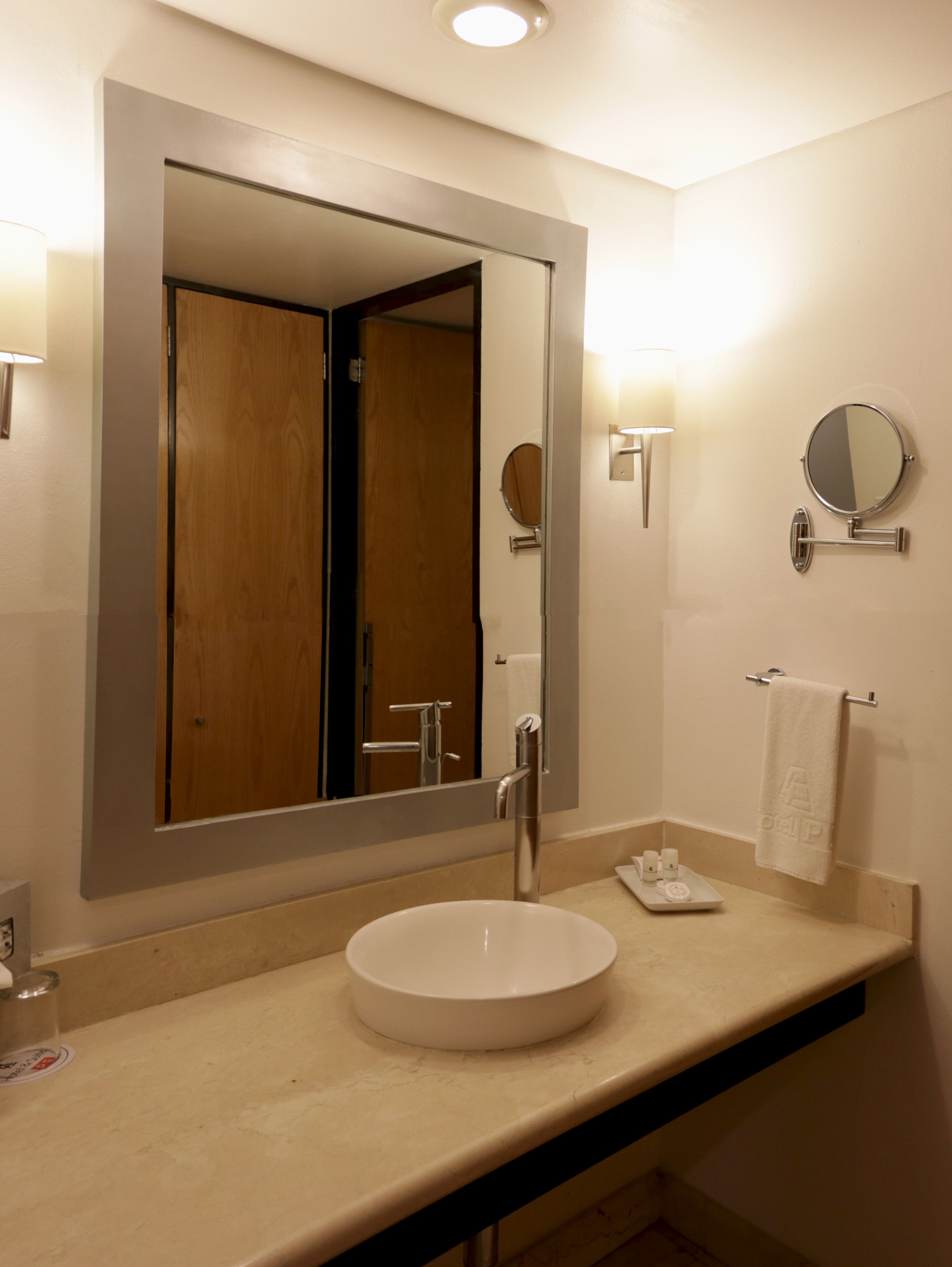 A modern bathroom with a large mirror, a round wall-mounted mirror, a white sink, and a towel rack.