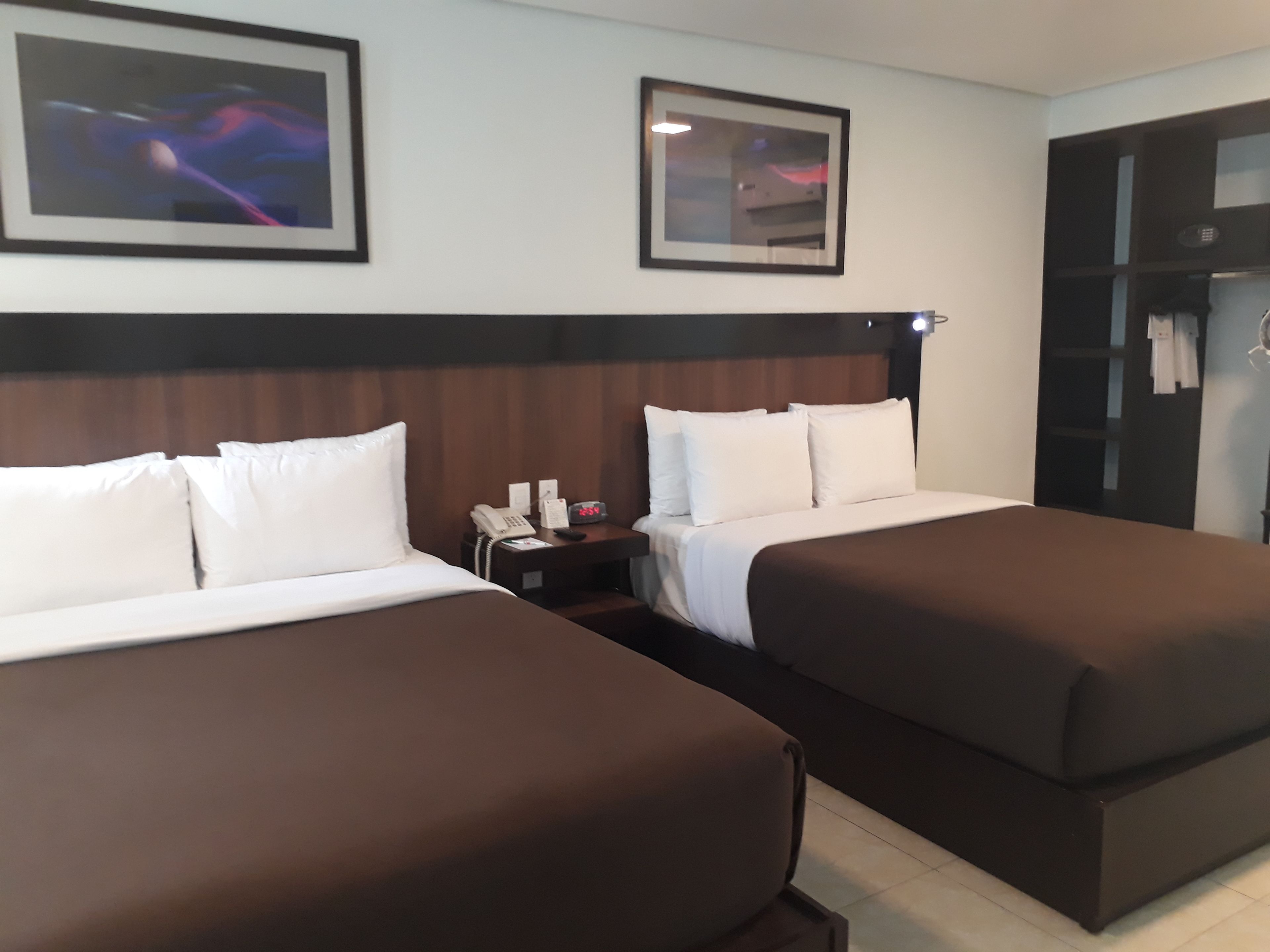 Ein Hotelzimmer mit zwei Betten, einem Nachttisch mit Telefon und Lampe sowie einem Kleiderschrank mit darin befindlicher Kleidung.