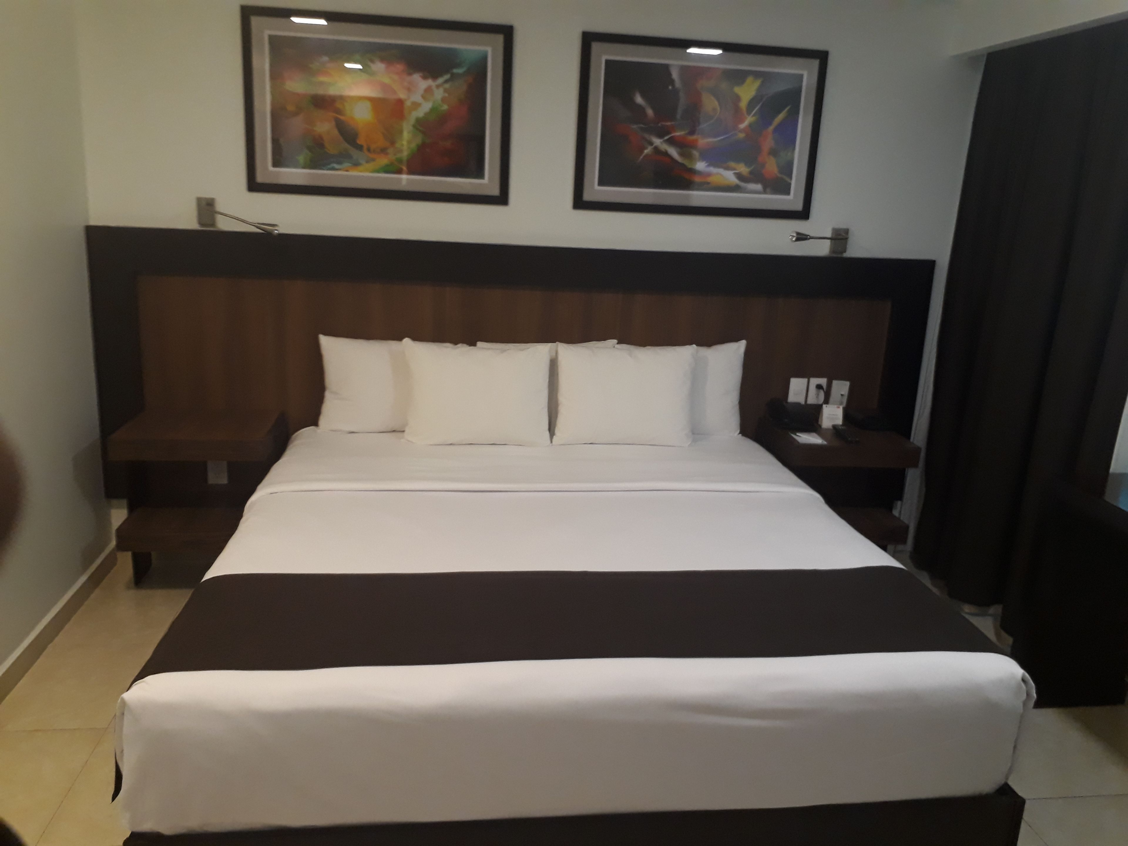 A hotel room with a large bed, two nightstands, and two abstract paintings on the wall.