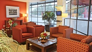 A hotel lobby with red sofas, a coffee table with flowers, a potted plant, and large windows.