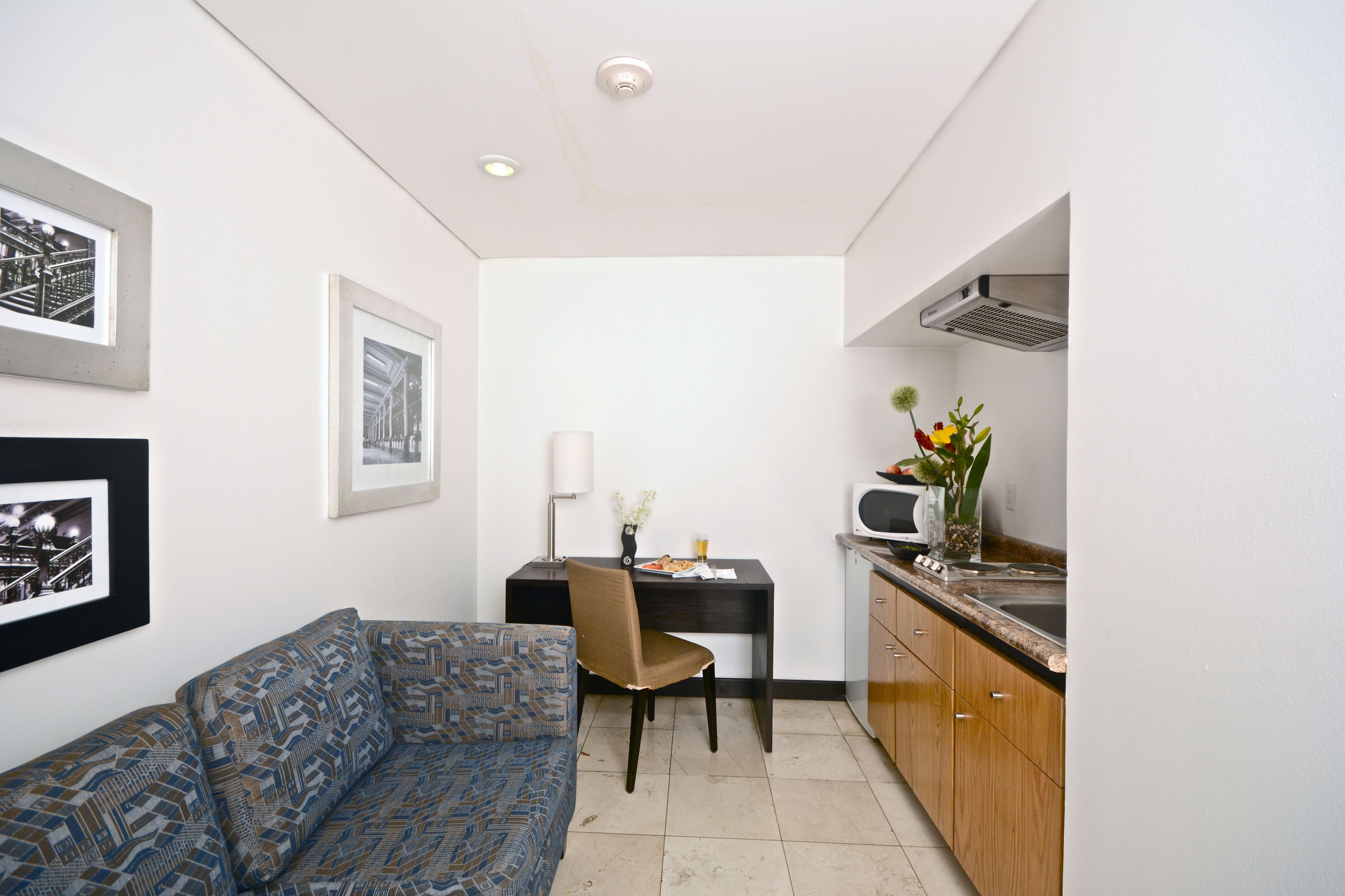 A compact living space with a sofa, a dining table with a chair, a kitchenette, and framed pictures on the walls.