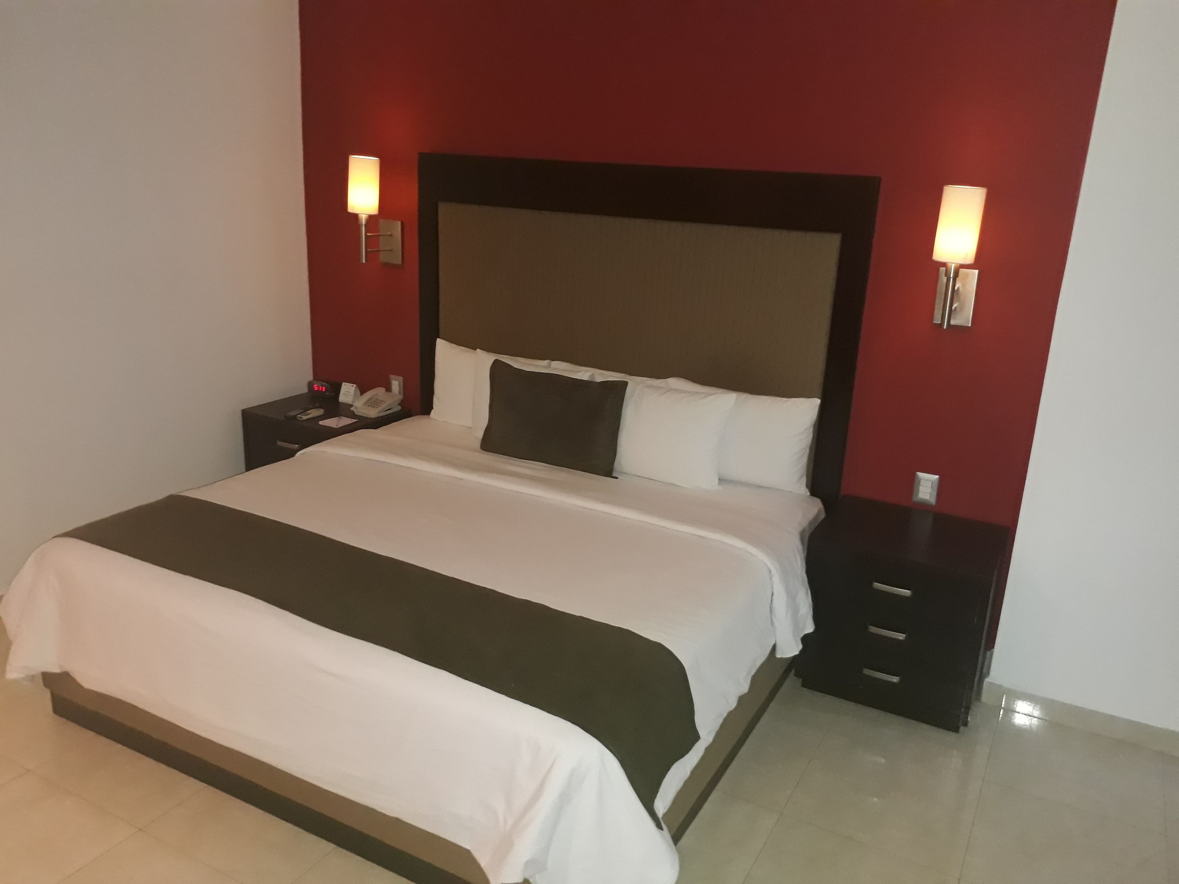 A neatly made bed with a white and dark-colored bedspread, two bedside tables with lamps, and a red accent wall.