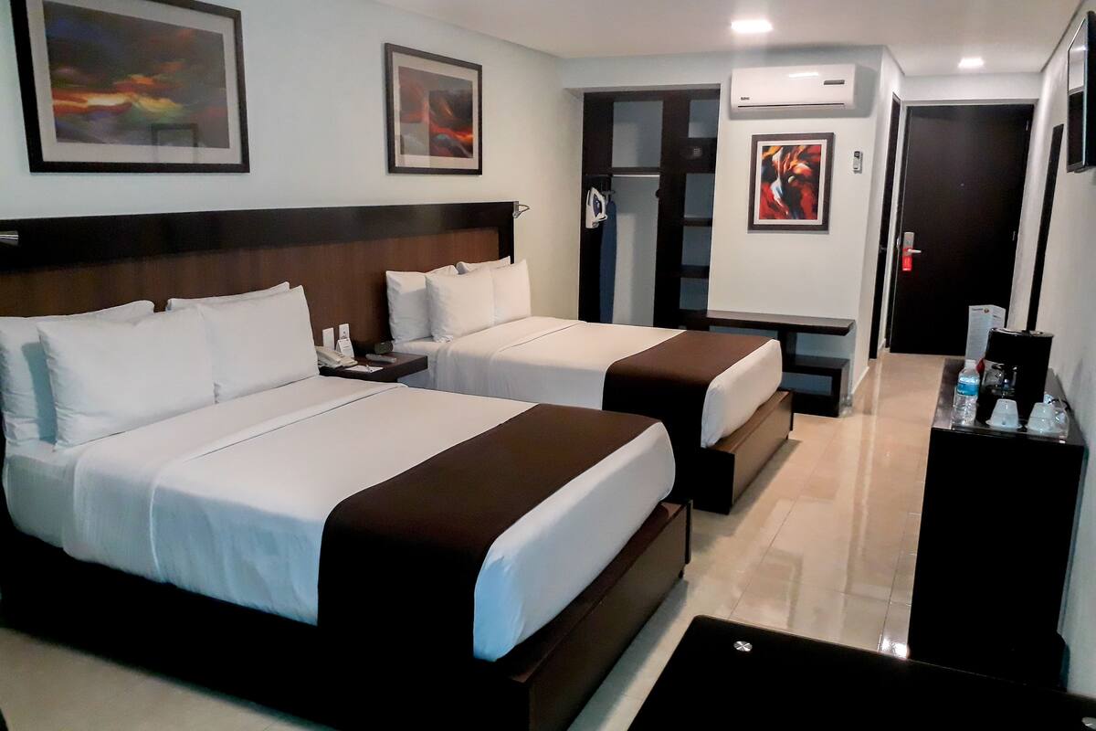 A hotel room with two beds, a desk, a coffee machine, and artwork on the walls.