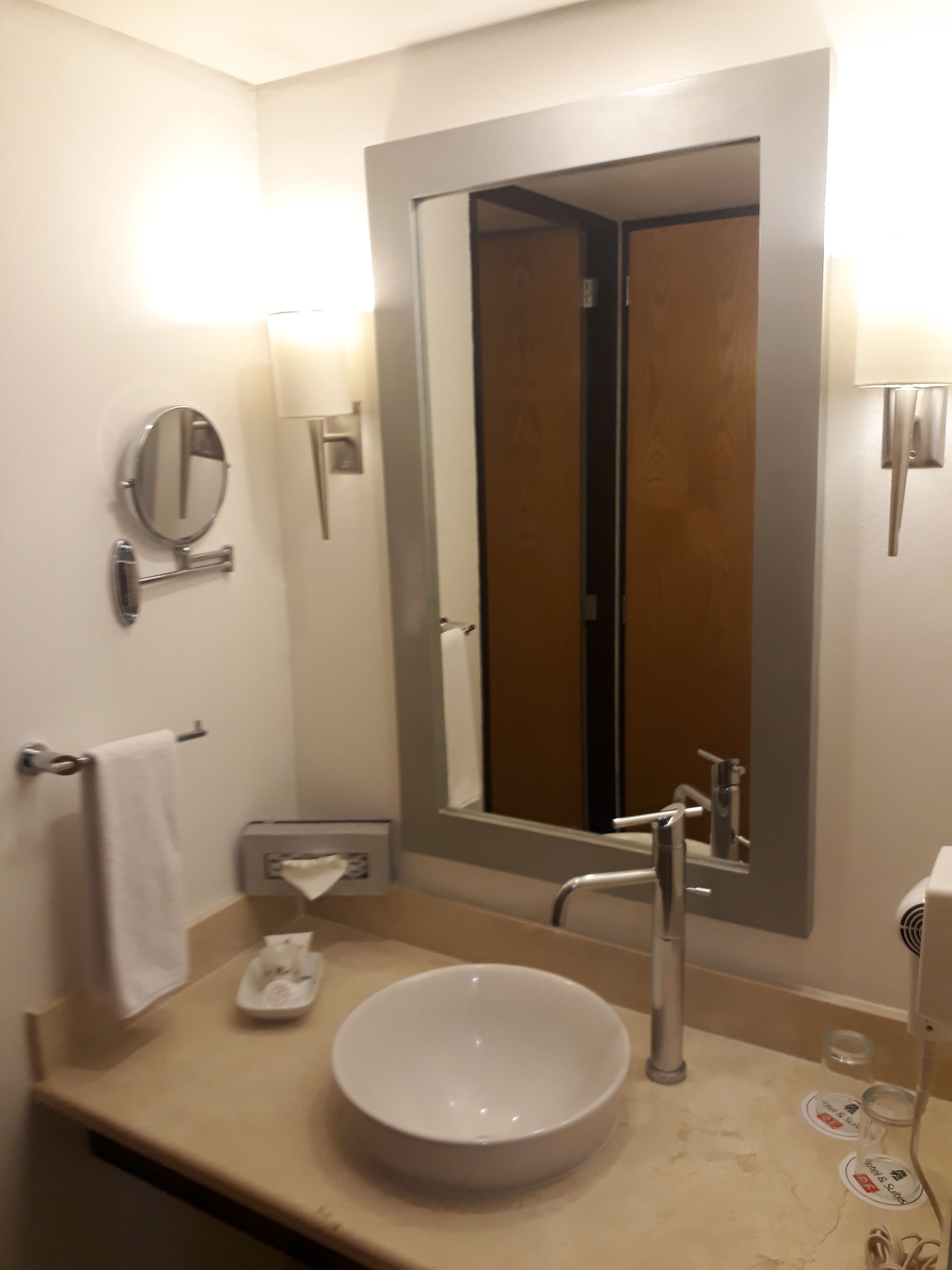 Un baño con un espejo grande, un lavamanos y un perchero para toallas.