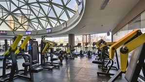 Een sportschool met diverse fitnessapparaten, een groot glazen dak en uitzicht op de stad.