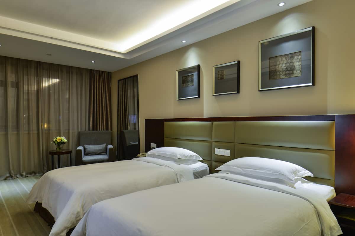 A hotel room with two beds, a chair, a small table with a vase of flowers, and artwork on the walls.