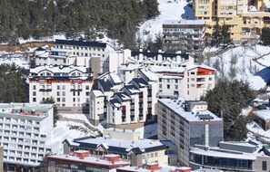 Une ville enneigée avec de nombreux bâtiments, dont un hôtel imposant doté d’une tour distinctive et un télésiège visible au loin.