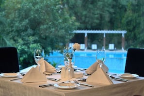 Ein Tisch ist für eine Mahlzeit gedeckt, mit Blick auf ein Schwimmbad und Grünflächen.