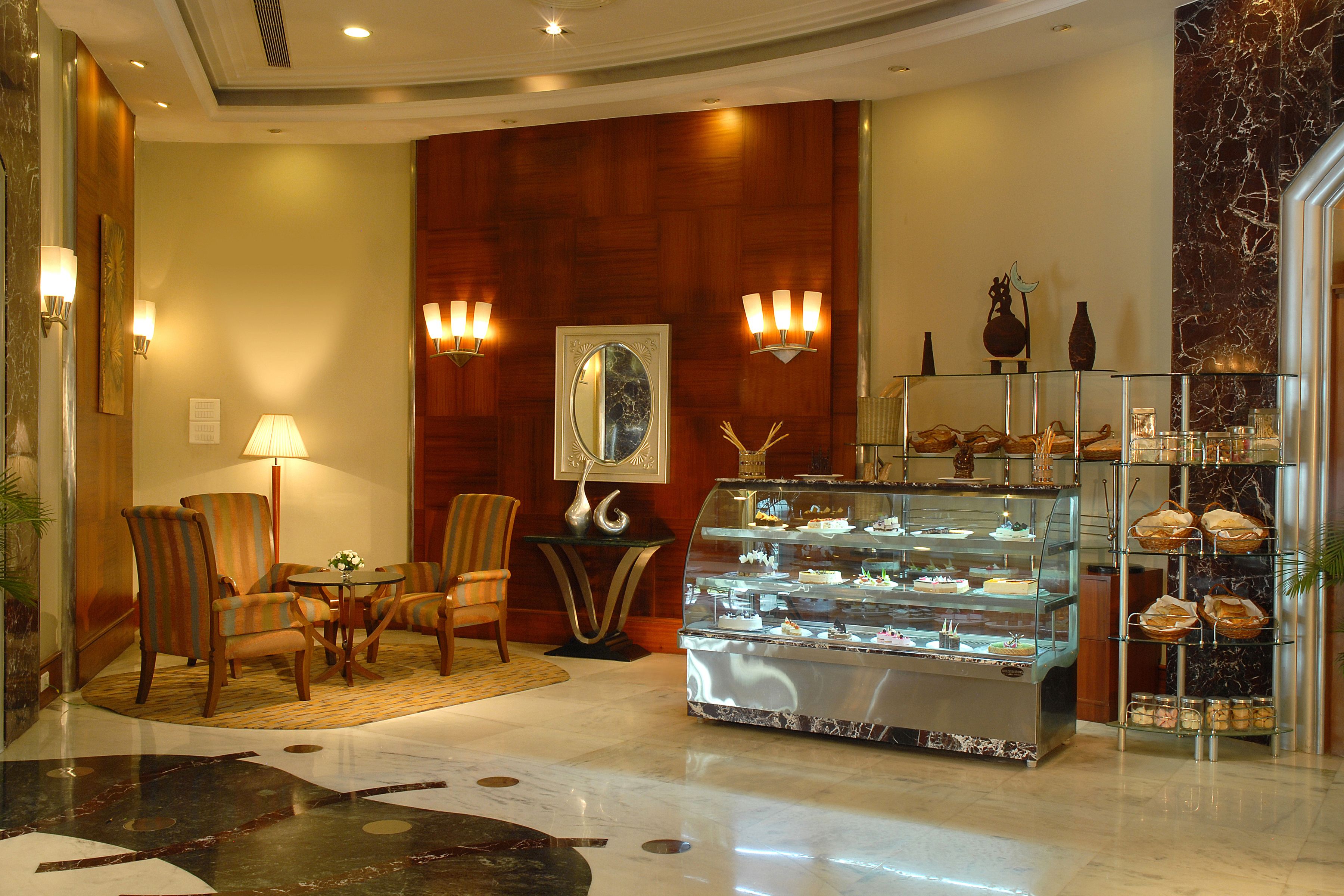 A lobby with a marble floor, a seating area with chairs, a glass display case with pastries, and wall sconces.