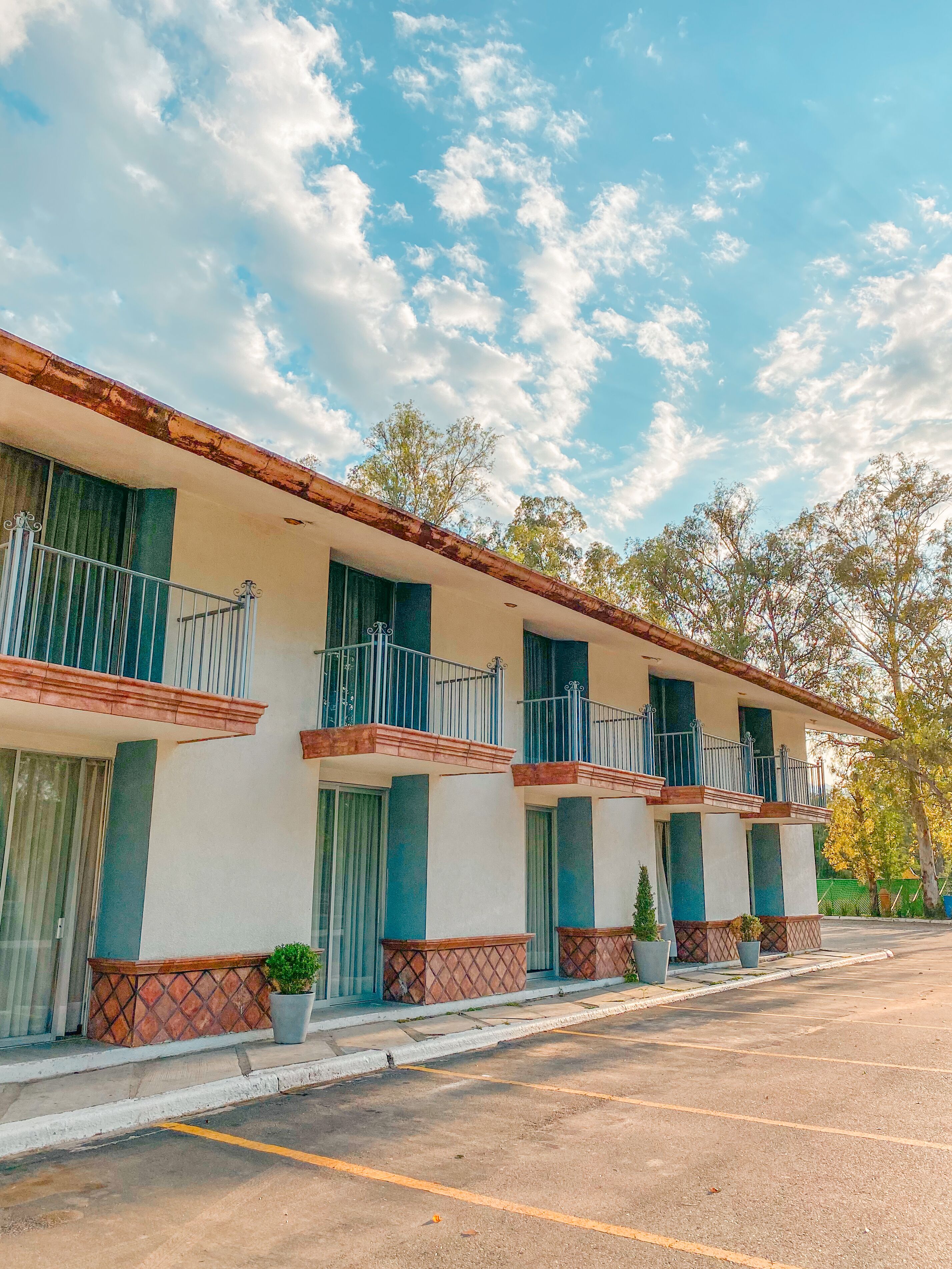 Une rangée de bâtiments de style motel, dotés de balcons, un parking et des arbres en arrière-plan.