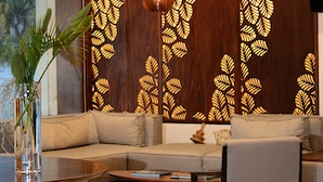 A modern living room with a sectional sofa, a coffee table, and a decorative wall with leaf patterns. - Gran Hotel Las Fuentes (Ciudad Victoria)