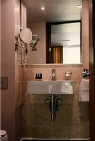 Un baño con un lavamanos blanco, un espejo y un perchero para toallas.
