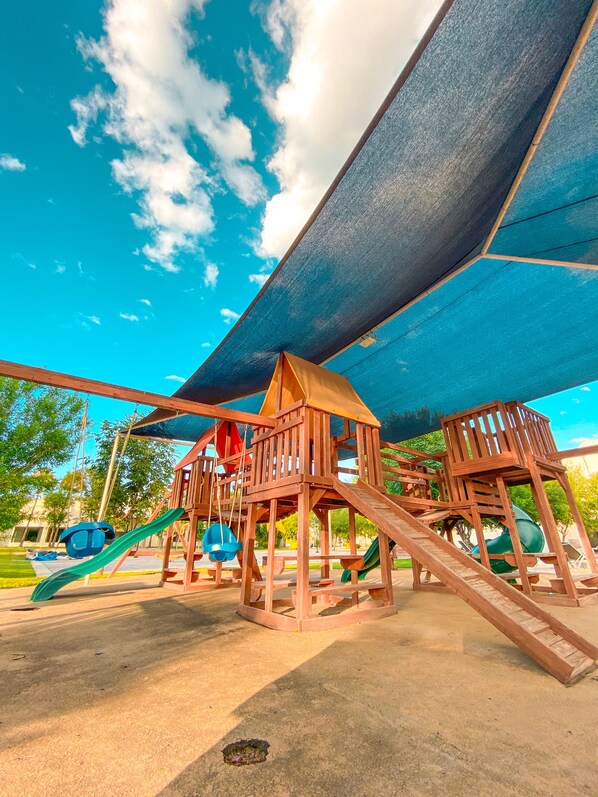 A playground with a wooden structure, slides, and a covered area.