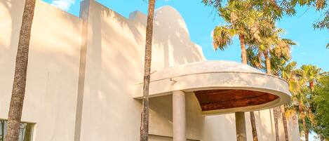 A modern building with a curved entrance, surrounded by palm trees and a clear sky.