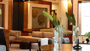 A modern hotel lobby with a sofa, chairs, a coffee table, and vases with plants. - Gran Hotel Las Fuentes (Ciudad Victoria)