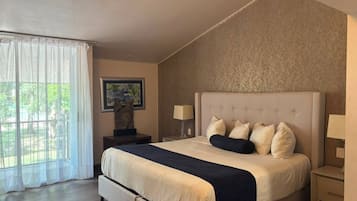 Quarto com cama grande, duas mesas de cabeceira, janela com cortinas e uma obra de arte na parede.