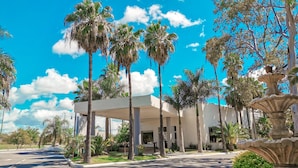 A modern building with a covered outdoor area surrounded by palm trees. - Gran Hotel Las Fuentes (Ciudad Victoria)