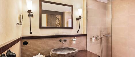 A bathroom with a stone sink, two wall-mounted lights, a large mirror, and a glass-enclosed shower.