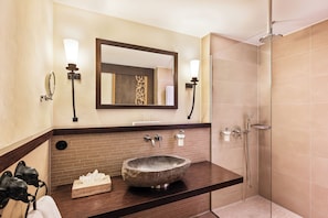 Een badkamer met een wastafel van steen, twee wandlampen, een grote spiegel en een douche met glazen wanden.