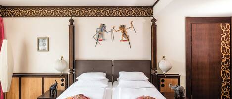 A double bed with an orange bedspread, two nightstands with lamps, a wooden headboard, and two wall-mounted decorative figures.