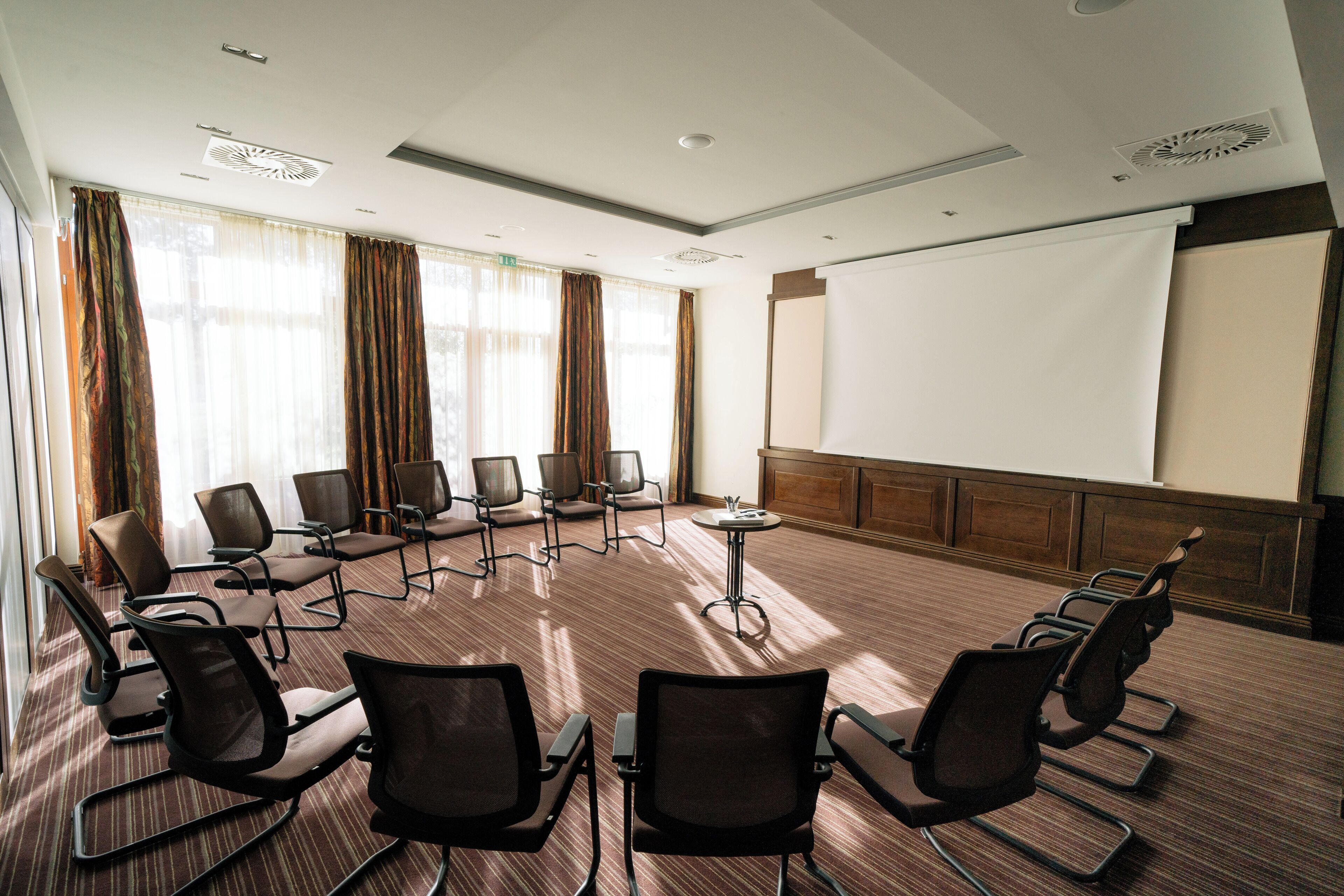 A conference room with a large screen, multiple chairs, and a carpeted floor.